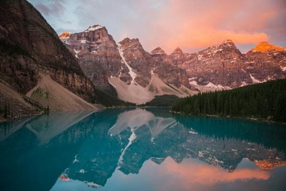 Mountain lake reflecting pink peaks at sunrise