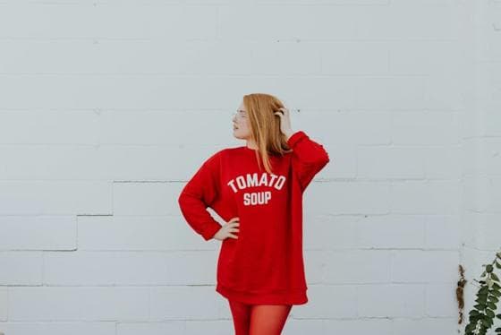 Woman in an oversized red sweater against a white wall